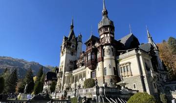 Peles Castle under a blue sky with mountains in the background.