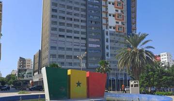 Tall modern building with a Senegal flag sculpture in front.