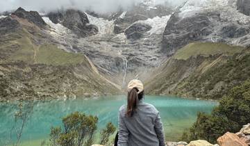 A person admiring a turquoise lake with mountain backdrop.