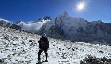 Hiker standing on a snowy terrain with majestic mountains under a deep blue sky.