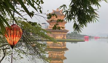 A pagoda reflected in water with lanterns hanging from trees.