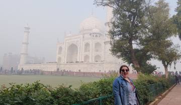 Woman smiling in front of the Taj Mahal on a foggy day.