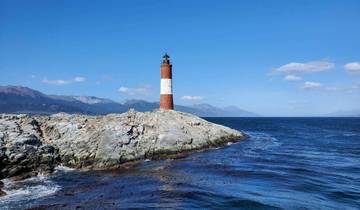 Lighthouse on a rocky shore with a mountainous backdrop.