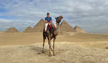 Man sitting on a camel with a backdrop of pyramids.