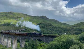 Steam train crossing a viaduct in a hilly, green landscape.