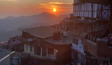Sunset view over a hilly cityscape with orange sky and silhouetted buildings.