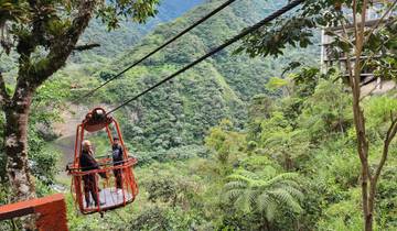 Two people in a cable basket crossing above a lush, mountainous landscape