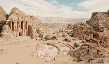 Ancient rock-hewn monastery in Petra surrounded by rocky landscape.