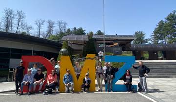 Tour group posing with large colorful letters spelling 'DMZ'.
