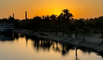 Sunset over a river lined with palm trees and boats.