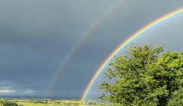Two rainbows forming over a lush green landscape.