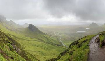 Vast green valley with winding road under a cloudy sky.