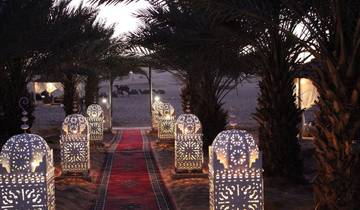 Desert camp with decorative lanterns and palm trees at dusk.