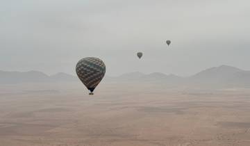 Hot air balloons floating over a desert with mountains in the background.