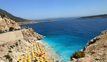 Crowded beach with parasols, blue sea, and cliffs.