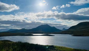 Lake with mountainous landscape under the sun and clouds.
