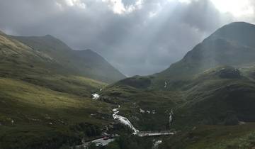 Dramatic landscape with a winding road and sunlight breaking through clouds.