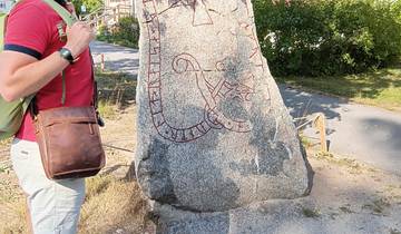 Person standing next to a runestone with carvings on a bright day.