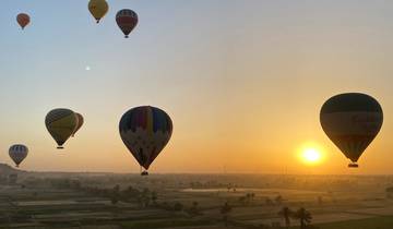 Hot air balloons floating in the air during sunrise over a landscape.