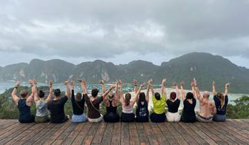People sitting on a deck overlooking a scenic bay with mountains.