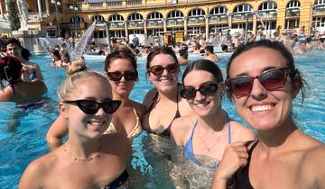 Five women posing in a swimming pool with people in the background.