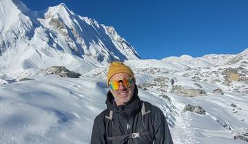 Man in winter gear standing against a snowy mountain backdrop.