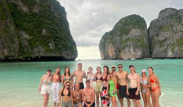 A large group of people posing at a beach with towering cliffs.