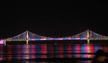 Illuminated bridge with colorful lights reflecting on the water at night.