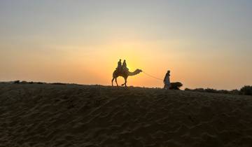 Silhouette of a camel and riders during sunset in a desert.