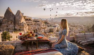 A woman enjoying breakfast with a view of Cappadocia and hot air balloons.