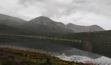 Mountain range reflected on calm water under overcast skies.