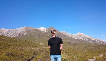 A person standing in front of a mountain range under a clear blue sky.