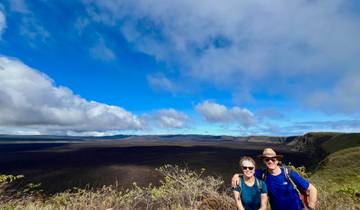 Two people posing in front of a vast landscape with a large crater under a blue sky.