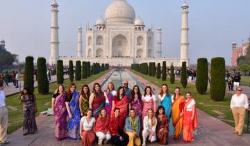 Group of tourists in front of the Taj Mahal, some wearing colorful saris.