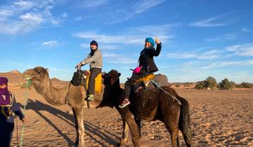 Two people riding camels in a desert landscape.