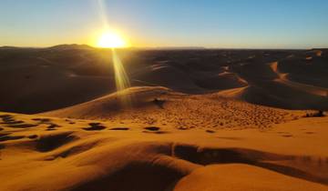 Sunset over sand dunes in a desert landscape.
