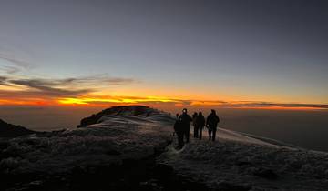 Silhouette of hikers on a snowy ridge during sunrise.