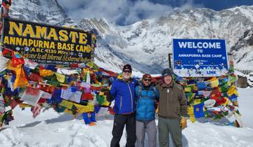 Three people standing at Annapurna Base Camp with flags.