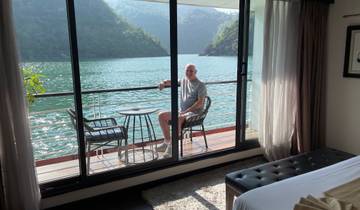Person sitting on a balcony of a cabin overlooking a scenic body of water.