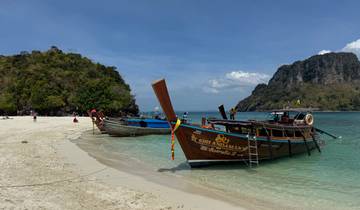 Traditional Thai boats on a sandy beach with clear blue water.