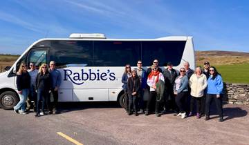 Group of tourists posing with a tour bus at a scenic location.