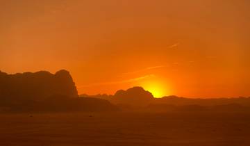 Sunset over desert landscape with silhouetted rocks.