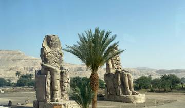 Two large stone statues with a palm tree in front.