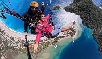 Two people paragliding over a coastal area with clear blue water.