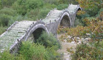 Stone bridge spanning across a river in a lush valley.