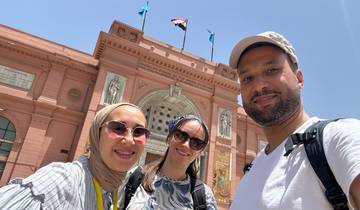 A group of people posing in front of a red historic building with flags.