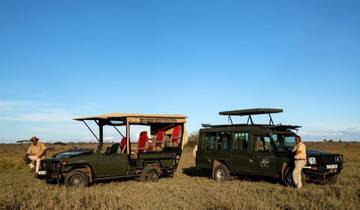 Two safari vehicles parked on a plain with people around