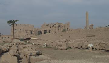 Large ancient ruins with columns and an obelisk under a blue sky.