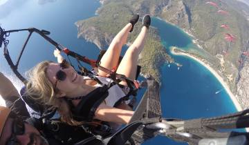 Person paragliding with a view of the coast and blue waters below.