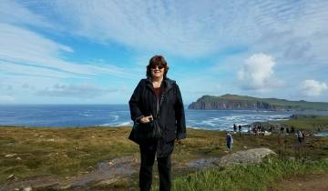 A person posing on a scenic coastal cliff.